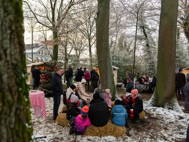 historischer-weihnachtsmarkt-bad-zwischenahn-stockbrot-am-tag.jpg Mensen zitten in de sneeuw rond een kampvuur en roosteren brood op stokjes op de kerstmarkt in Bad Zwischenahn.