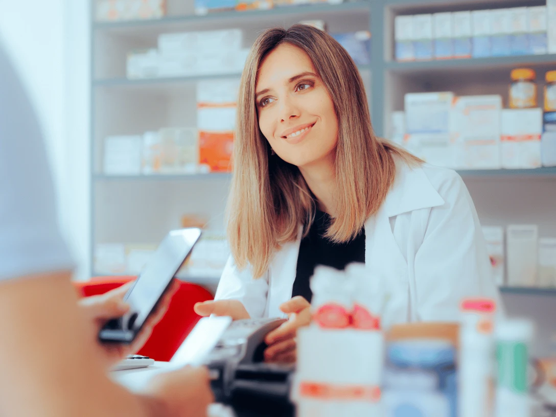 Apotheke auf der Lohe.png Auf dem Bild ist eine freundliche Apothekerin zu sehen, die ein Kundengespräch führt. Der Kunde möchte gerade kontaktlos mit seinem Handy bezahlen. Im Hintergrund sind Regale mit weiteren Produkten sichtbar.