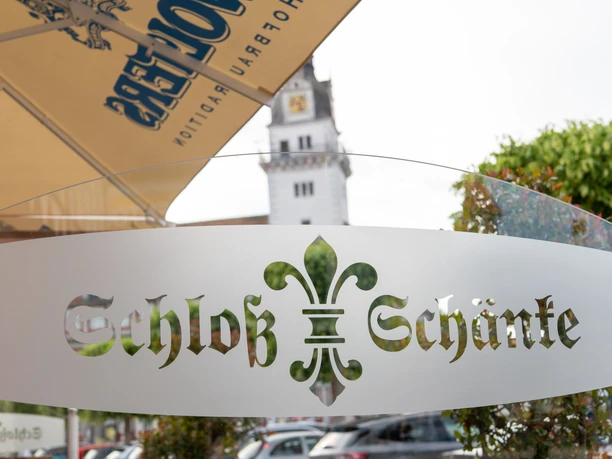 Schloss-Schänke Logo Schloss-Schänke Logo Schriftzug auf halb-durchsichtiger Glassscheibe. Im Hintergrund verschwommen der Schlossturm.