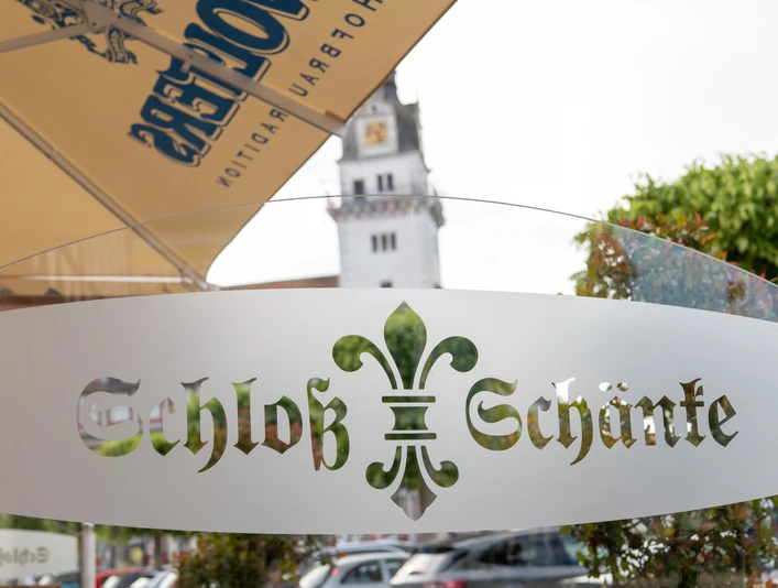 Schloss-Schänke Logo Schloss-Schänke Logo Schriftzug auf halb-durchsichtiger Glassscheibe. Im Hintergrund verschwommen der Schlossturm.