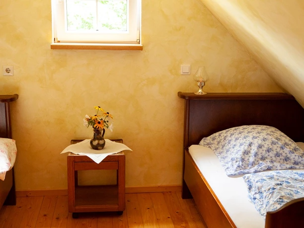Two rustic single beds with floral cushions in a room with a sloping roof and small window.