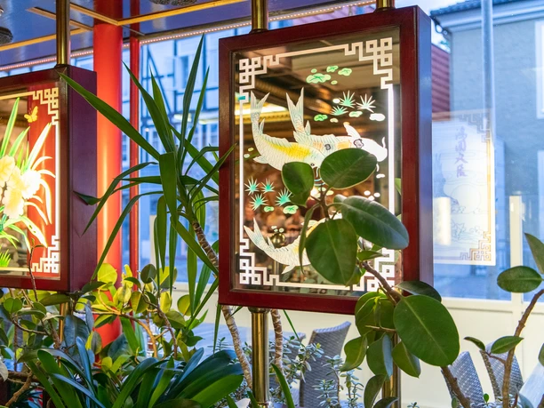 Wan Bao Wan Bao Fensterdekoration mit leuchtenden Bildern von Fischen und Blumen. Darum viele Zimmerpflanzen.