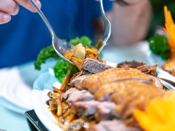 Wan Bao Gericht Nahaufnahme eines länglichen Tellers mit Entenfleischstücken. Mit Gabel und Löffel wird ein Stück heruntergenommen.