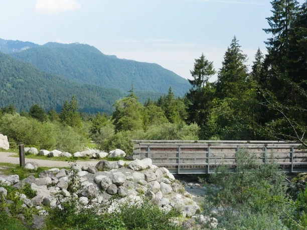 Farchant Natur- und Erholungspark Kuhflucht Fußgängerbrücke über Bach in bewaldeter Berglandschaft mit Fahrradweg.
