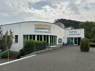 Hallenbad Badino <p>Modernes Freizeitbad mit weißer Fassade in einer grünen Umgebung unter bewölktem Himmel.</p>
