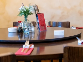 Wok In: Am Tisch Runder, dunkler Tisch mit Besteck, Sojasoße, Blumendeko