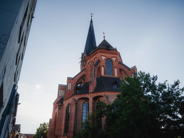 The red-brick St. Nicolai Church in Lüneburg, with its pointed tower, under a blue sky.