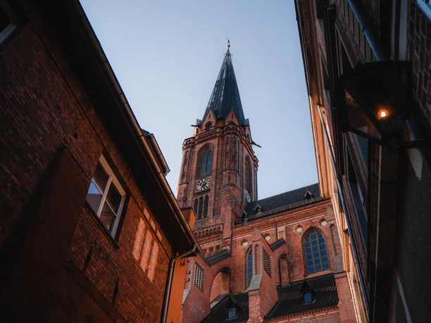A view through a narrow alley of the brick tower of St. Nicholas Church in Lüneburg.