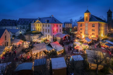 Een feestelijk verlichte kerstmarkt in de vesting Königstein met talrijke marktkraampjes.