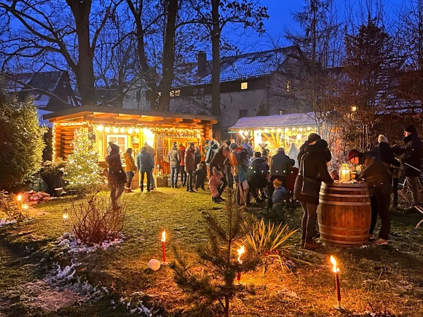 Festively illuminated Christmas market with people in front of a wooden hut in the evening winter atmosphere.