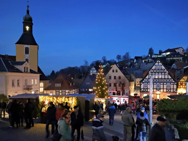 Weihnachtsmarkt Hohnstein Weihnachtsmarkt in Hohnstein bei Dämmerung, mit erleuchtetem Baum und Besuchern, umgeben von Fachwerkhäusern.