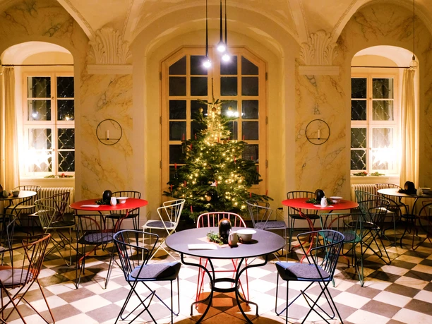 A festively lit room with a festively decorated tree and attractively laid tables.