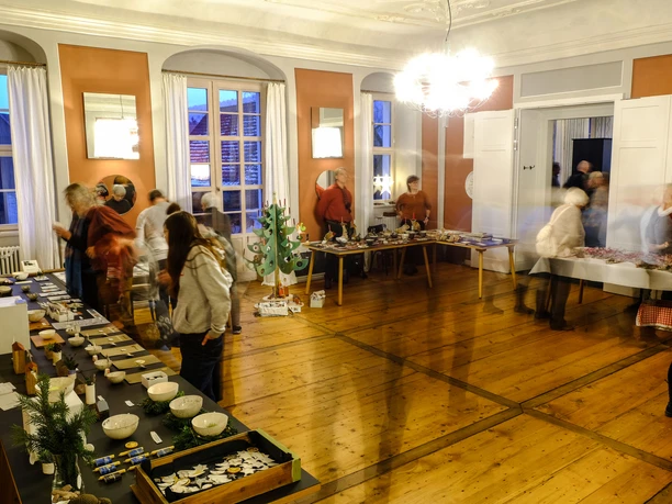 Schloss Prossen Adventsmarkt Menschen besuchen den Schloss Prossen Adventsmarkt, um handgefertigte Waren in einem festlichen Raum zu erkunden.