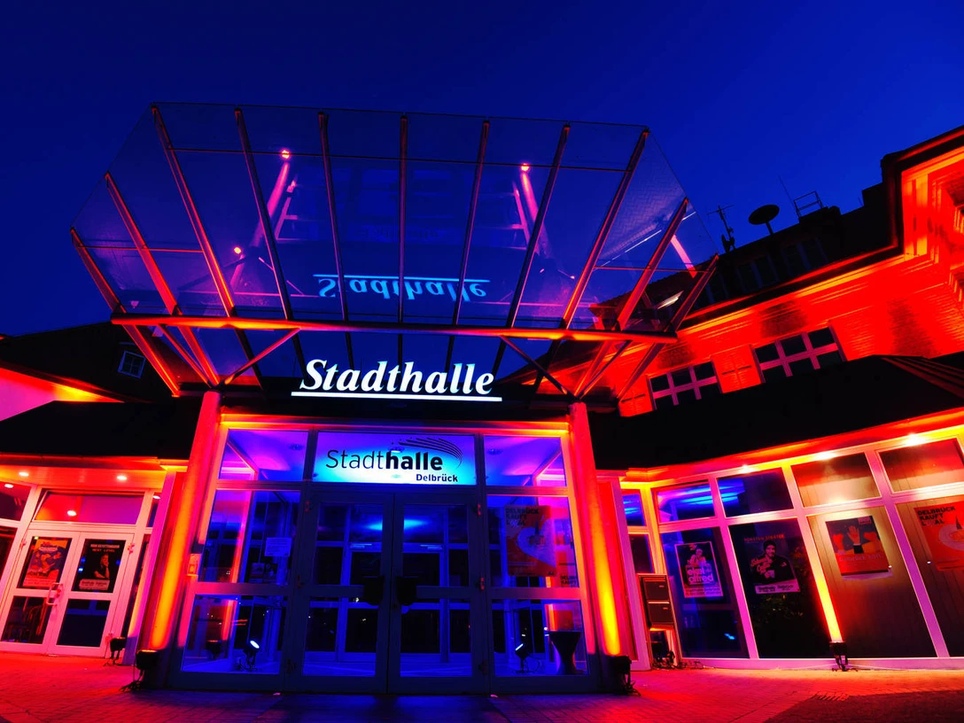 Delbrueck_Stadthalle_Außenansicht beleuchtet Stadthalle Delbrück ist nachts eindrucksvoll beleuchtet, Glasfassade und Schriftzug erstrahlen hell.
