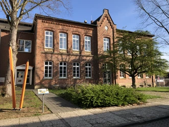 Grönebergschule Melle.jpg Backsteingebäude mit großen Fenstern, grüne Bäume im Vordergrund, blauer Himmel.