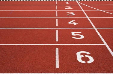 Rote Tartanbahn mit sechs nummerierten Startlinien in einem Stadion für Leichtathletikveranstaltungen.