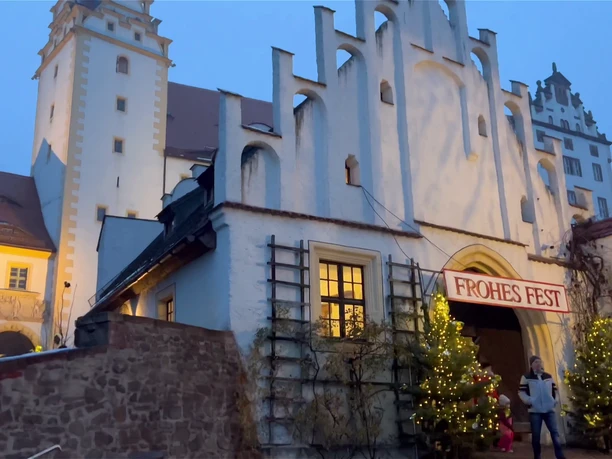 You can see the entrance to Colditz Castle. Two decorated Christmas trees have been placed at the entrance gate and a banner with the words "Merry Christmas" hangs above the door