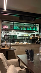 Oase Theke.jpg Eine gemütliche Bar mit zahlreichen Flaschen und Gläsern, die hinter einem Tresen mit Hockern stehen.