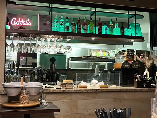 Oase Theke.jpg Eine gemütliche Bar mit zahlreichen Flaschen und Gläsern, die hinter einem Tresen mit Hockern stehen.