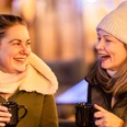 Glühwein trinken auf dem Weihnachtsmarkt Zusehen sind zwei Frauen die jeweils eine Glühweintasse in der Hand halten und lachen.