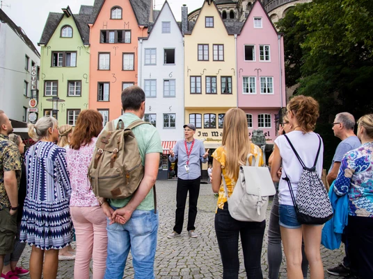 Guided tour of the fish market in Cologne's old town Eine Gruppe von Menschen steht am historischen Fischmarkt in Köln. Im Hintergrund sind bunte Fachwerkhäuser zu sehen, die eine lebendige und einladende Kulisse bilden.A group of people stand at the historic fish market in Cologne. Colorful half-timbered houses can be seen in the background, creating a lively and inviting backdrop.