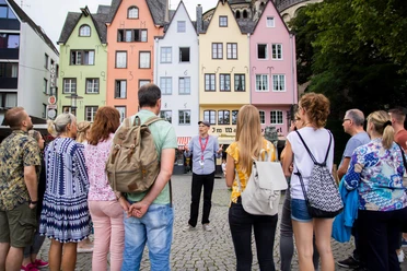 Stadtführung auf dem Fischmarkt in der Kölner Altstadt Eine Gruppe von Menschen steht am historischen Fischmarkt in Köln. Im Hintergrund sind bunte Fachwerkhäuser zu sehen, die eine lebendige und einladende Kulisse bilden.