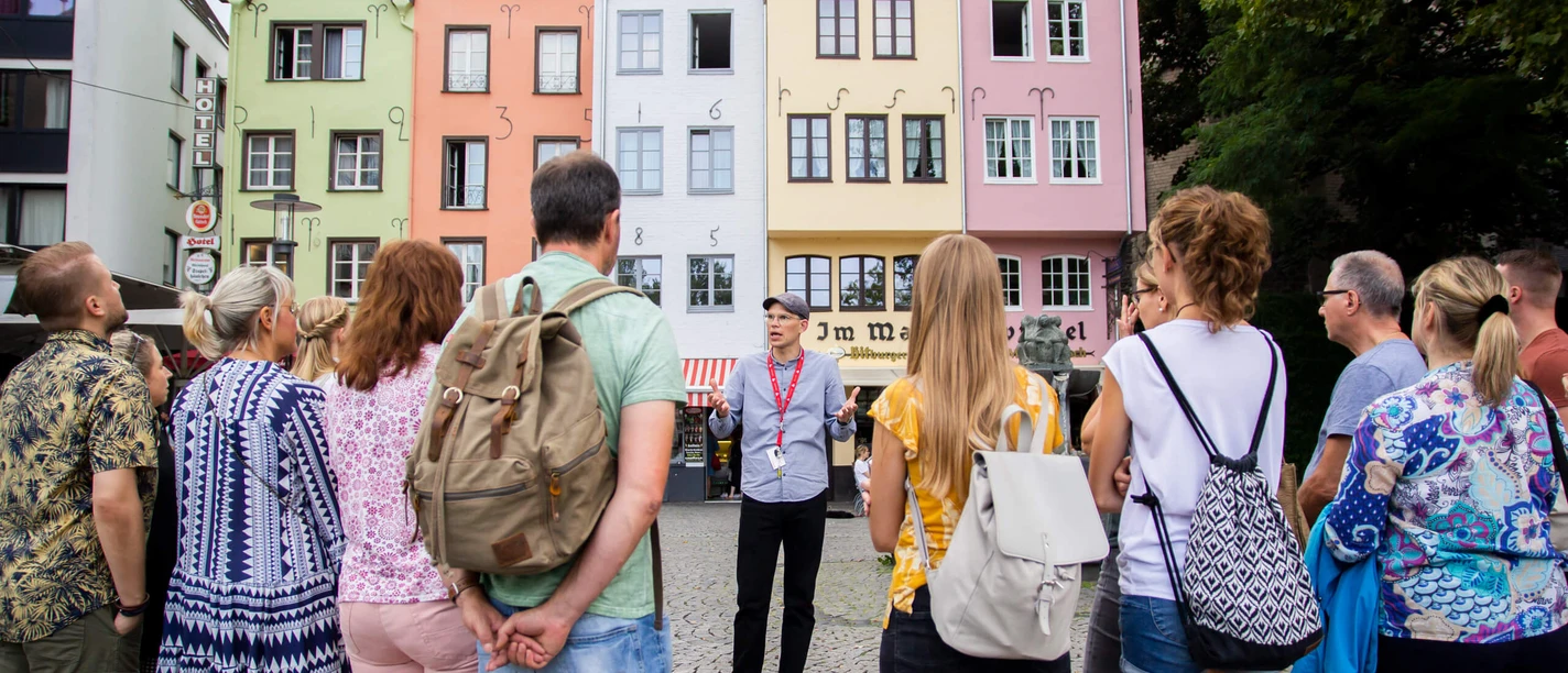 Stadtführung auf dem Fischmarkt in der Kölner Altstadt Eine Gruppe von Menschen steht am historischen Fischmarkt in Köln. Im Hintergrund sind bunte Fachwerkhäuser zu sehen, die eine lebendige und einladende Kulisse bilden.