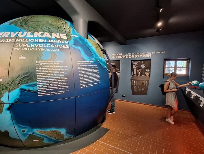 1 - Supervulkan-Zentrum R├Âcknitz - Dauerausstellung - Foto Kathleen Schramm.jpg Ausstellung mit Infotafeln über Supervulkane und tektonische Platten. Besucher erkunden Exponate.Exhibition with information boards about supervolcanoes and tectonic plates. Visitors explore exhibits.Výstava s informačními tabulemi o supervulkánech a tektonických deskách. Návštěvníci si prohlédnou exponáty.Wystawa z tablicami informacyjnymi o superwulkanach i płytach tektonicznych. Odwiedzający zwiedzają eksponaty.Tentoonstelling met informatieborden over supervulkanen en tektonische platen. Bezoekers verkennen de tentoongestelde stukken.Mostra con pannelli informativi sui supervulcani e sulle placche tettoniche. I visitatori esplorano gli oggetti esposti.
