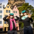 TimeRide VR Altstadttour Zwei lächelnde Personen mit VR-Brillen vor bunten Stadthäusern und einer Kirche.Two smiling people with VR glasses in front of colorful townhouses and a church.