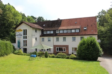 Ein mehrstöckiges Landhotel mit roten Dachziegeln, umgeben von einem gepflegten Garten und Bäumen.