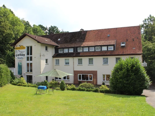 Ein mehrstöckiges Landhotel mit roten Dachziegeln, umgeben von einem gepflegten Garten und Bäumen.