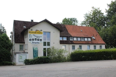 Zweistöckiges Gebäude mit weißer Fassade und rotem Dach; ein Café-Schild prangt oberhalb des Eingangs.