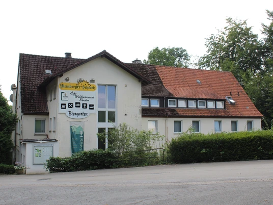 Zweistöckiges Gebäude mit weißer Fassade und rotem Dach; ein Café-Schild prangt oberhalb des Eingangs.