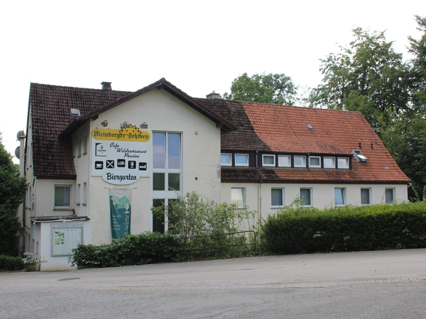 Zweistöckiges Gebäude mit weißer Fassade und rotem Dach; ein Café-Schild prangt oberhalb des Eingangs.