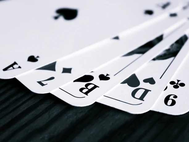 Spielkarten mit Pik-Ass, Kreuz-Neun, Karo-Zwei, Pik-Bube und Pik-Dame auf dunkler Holzfläche.