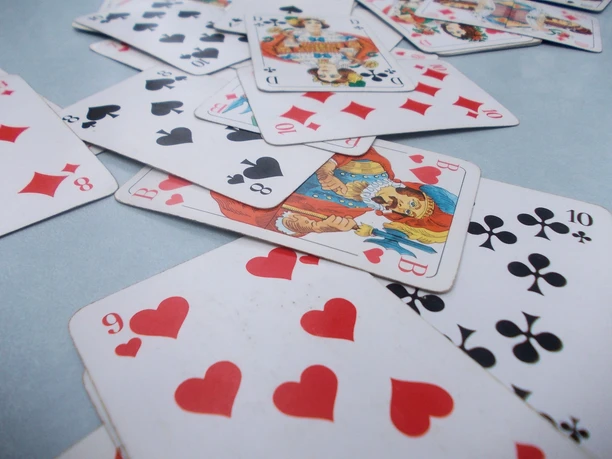 Spielkarten mit Herz, Pik, Kreuz und Karo liegen durcheinander auf einem hellen Untergrund.
