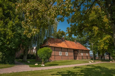 Torhaus Lengerich (c) Karin Knus.jpg Backsteinbau mit rotem Ziegeldach im Grünen, umgeben von alten Bäumen und gepflegten Wegen.
