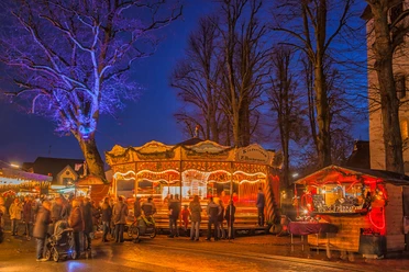 Beleuchtetes Karussell und Marktstände mit Besuchern auf dem Hamberger Weihnachtsmarkt bei Nacht.