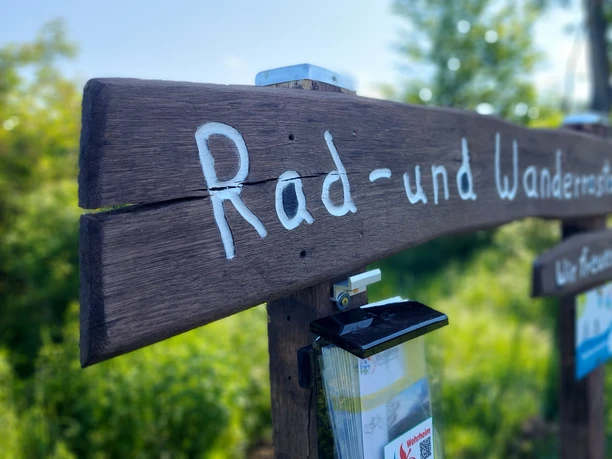 Der Klimaerlebnispfad ist Rad- und Wanderweg Holzschild mit der Info Rad- und Wanderweg. Darunter ist ein Kasten mit Infoflyern montiert.