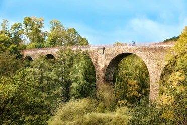 Viadukt Ruhrstraße Süd, Heiligenhaus Steinviadukt mit hohen Bögen überspannt eine bewaldete Schlucht, Radfahrer auf der Brücke.