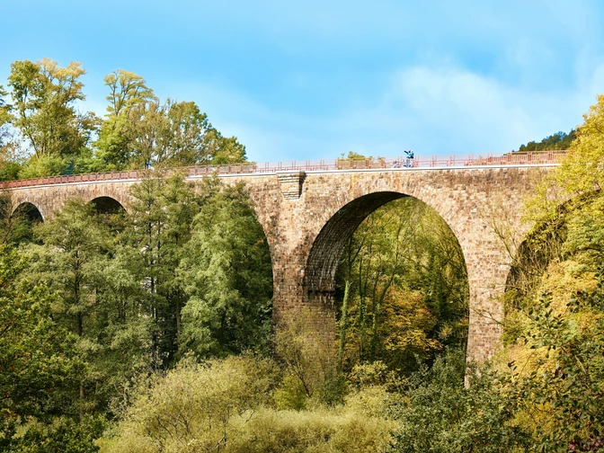 Viadukt Ruhrstraße Süd, Heiligenhaus Steinviadukt mit hohen Bögen überspannt eine bewaldete Schlucht, Radfahrer auf der Brücke.