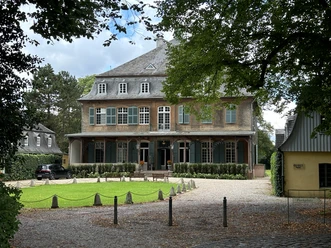 Schloss Eicherhof Herrschaftliches Backsteingebäude mit grünen Fensterläden und begrüntem Hof vor bewaldeter Kulisse.