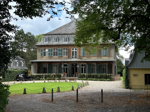 Schloss Eicherhof Herrschaftliches Backsteingebäude mit grünen Fensterläden und begrüntem Hof vor bewaldeter Kulisse.