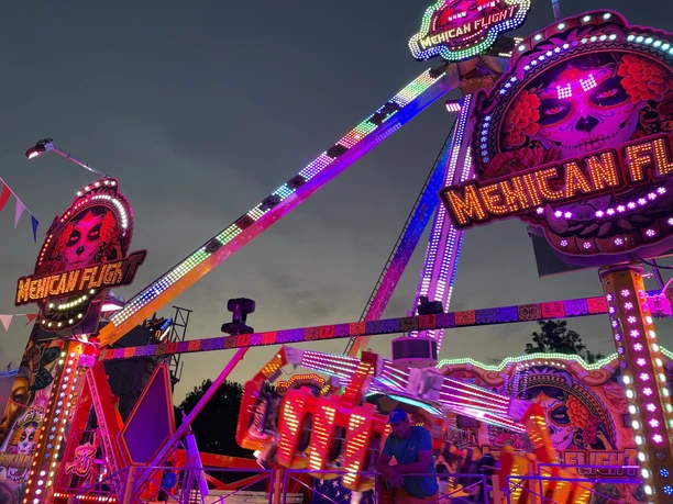 Günzburger Volksfest Eine farbenfrohe Bühne auf dem Günzburger Volksfest zeigt ein strahlendes Fahrgeschäft bei Dämmerung.