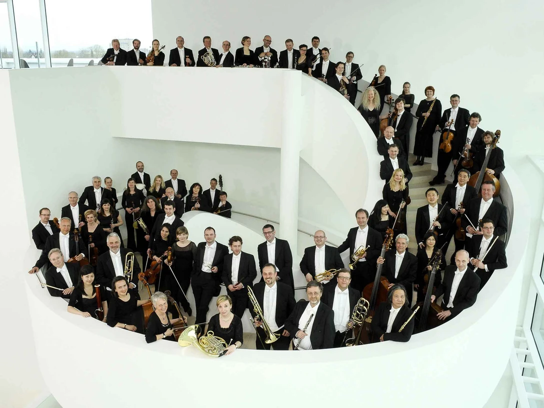 TWT_NWD_2013_2_c_sandra_kreutzer.jpg Ein großes Orchester in schwarzer Abendgarderobe posiert auf einer weißen Wendeltreppe.