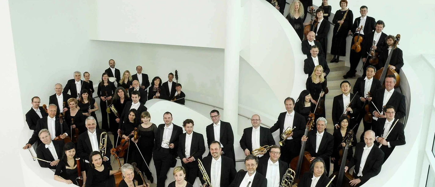 TWT_NWD_2013_2_c_sandra_kreutzer.jpg Ein großes Orchester in schwarzer Abendgarderobe posiert auf einer weißen Wendeltreppe.