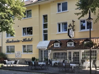 Hotel Front mit Teutonia Schild.JPG Das Teutonia Hotel mit gelber Fassade und beschattetem Außenbereich lädt zum Verweilen ein.