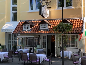 Aussenanstrich detailled shot.jpg Ein kleines Restaurant mit rötlichem Ziegeldach und gemütlicher Terrasse mit gedeckten Tischen.