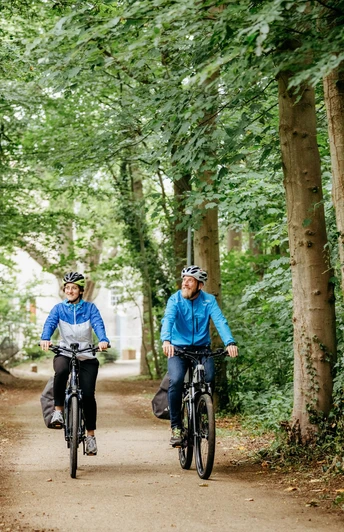 Brückenradweg Osnabrück - Bremen Zwei Radfahrer genießen eine Fahrt auf einem Waldweg, umgeben von hohen Bäumen.