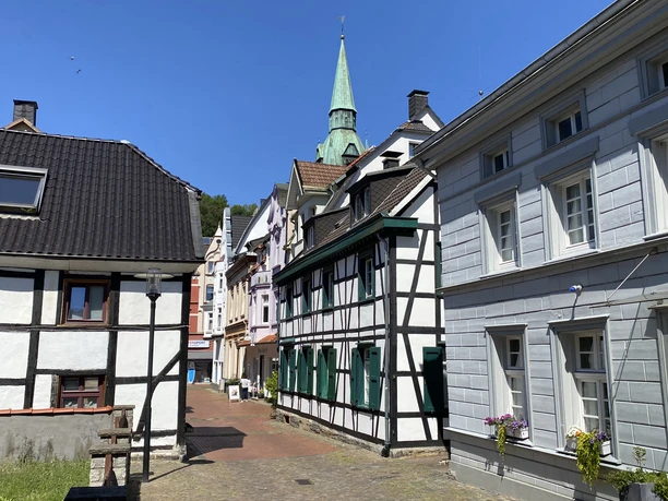 IMG_0904.jpg In einem historischen Stadtkern mit Fachwerkhäusern erstreckt sich eine gepflasterte Gasse unter blauem Himmel.